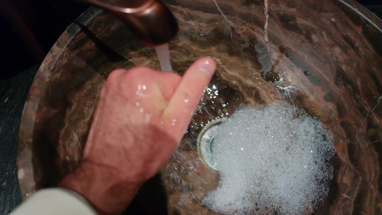 Persona lavándose las manos con jabón bajo el agua corriente en un lavabo.