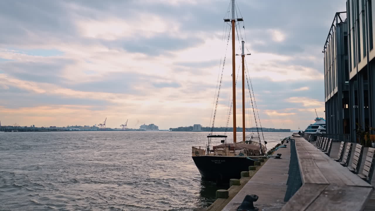 New York, ABD, 9 Aralık 2025: Yelkenleri indirilmiş yelkenli tekne iskelede duruyor. Arka planda gri bulutlu gökyüzü ve çalkantılı deniz manzarası.