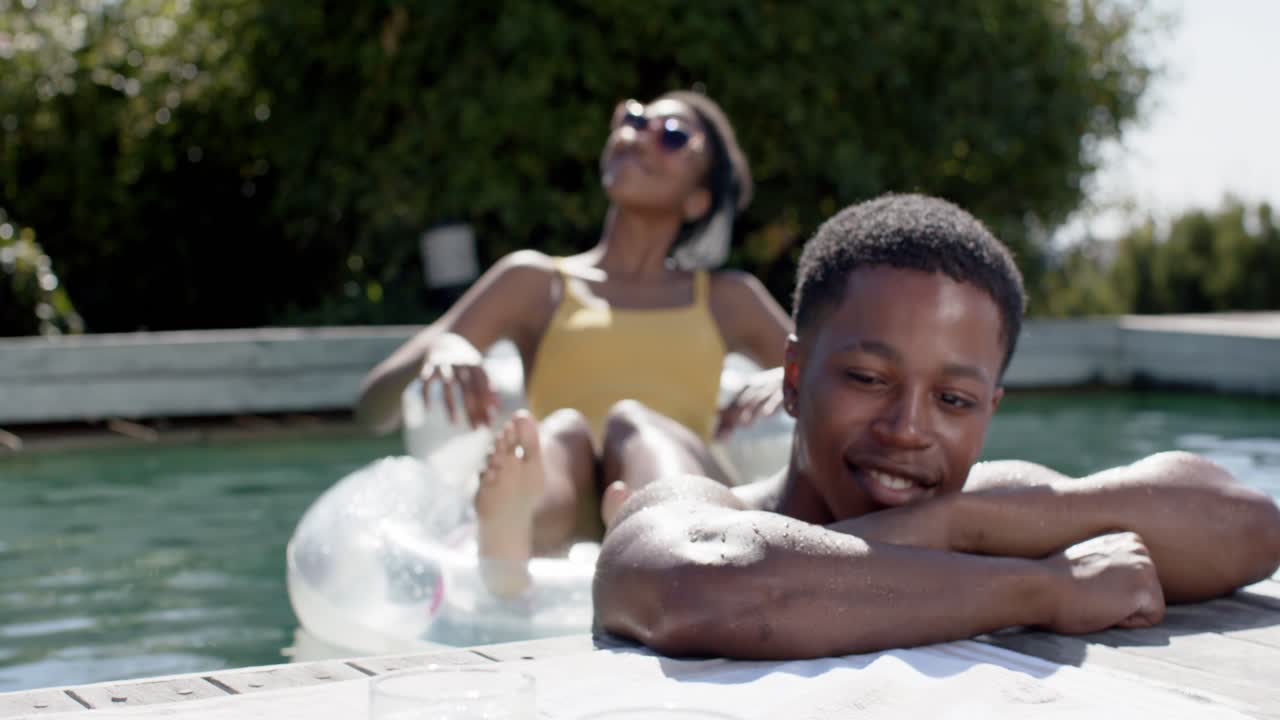 Couple at pool edge, man leaning smiling, woman reclining in yellow swimsuit soaking sun, glasses