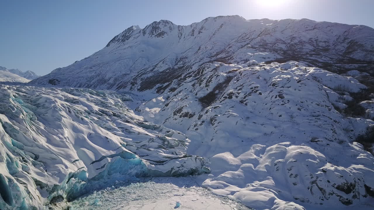 눈 속에 주차된 전경의 비행기를 드러내기 위해 빙하의 측면을 비행하는 공중