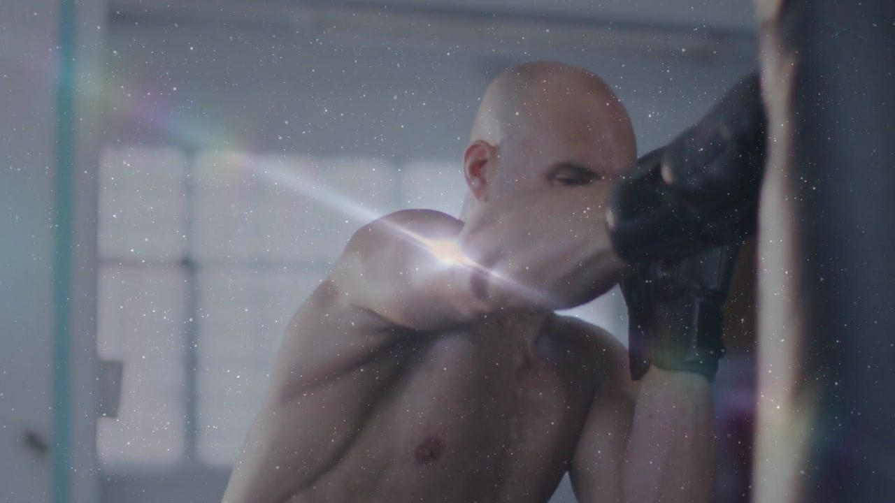 Male boxer starting tightguard jab combo on heavy bag for training, gloves flashing lensflare dust