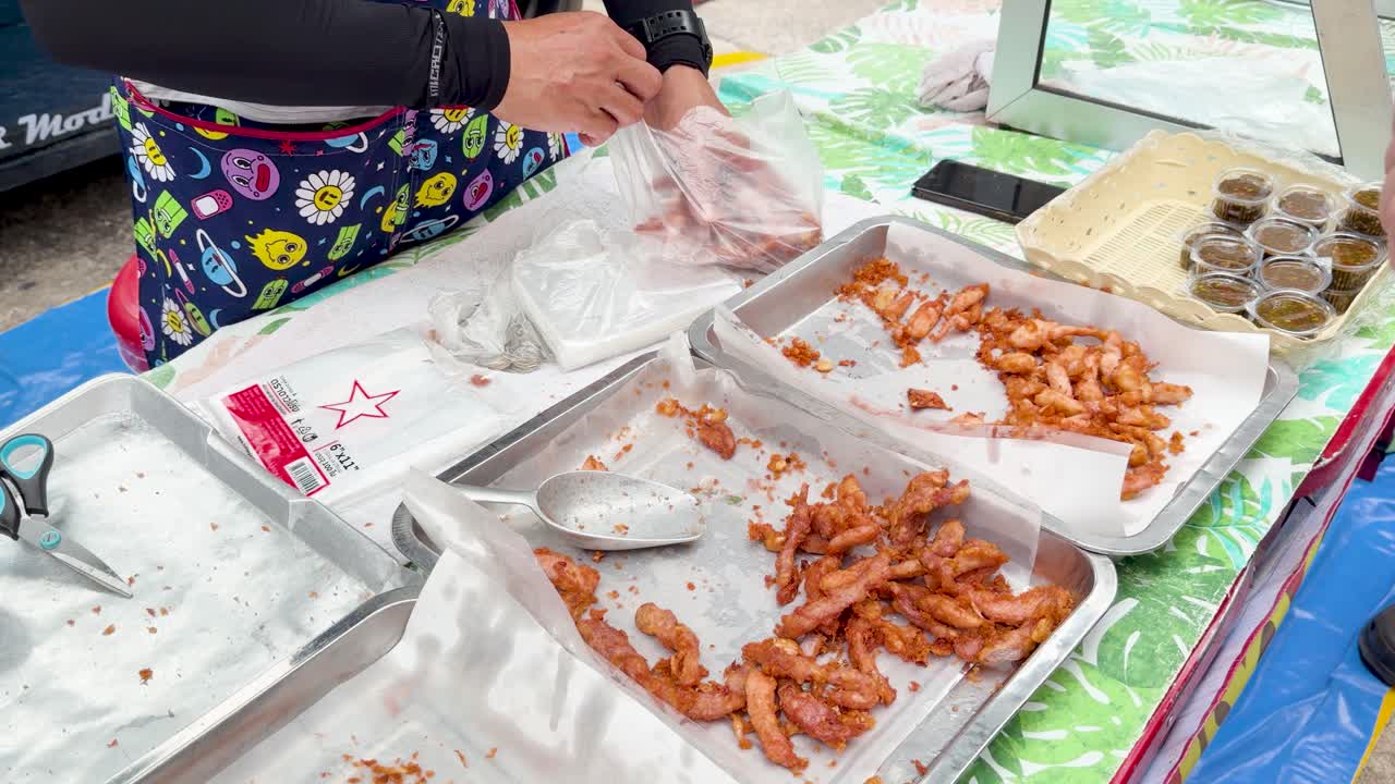 Vendor packs fried chicken and pork for customer at busy outdoor market in Thailand