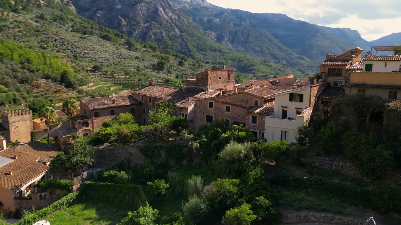 Una vista incantevole di Fornalutx, Maiorca, che mostra case tradizionali in pietra, vegetazione lussureggiante e uno sfondo montuoso bagnato dal sole