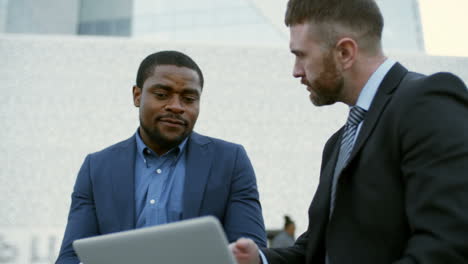 and businessmen sitting outdoors, looking at laptop screen and discussing some issues 1