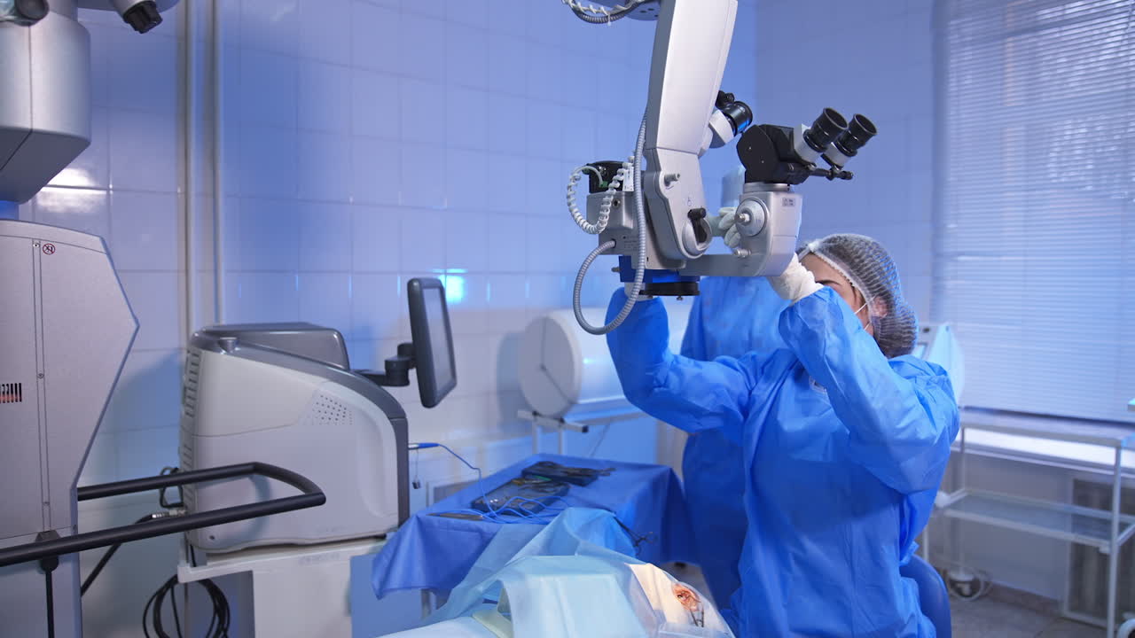 Preparation for eye surgery. Female doctor in mask and hat adjusts equipment over the patient on surgery table.
