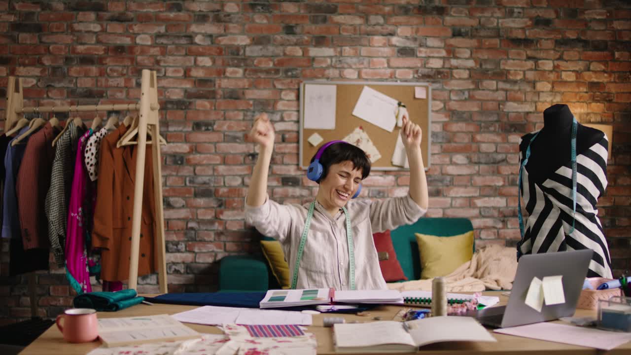 atractiva mujer diseñadora de moda feliz y emocionada con una gran sonrisa escuchando música de los auriculares en su taller de costura y vomitó los botones. 4k