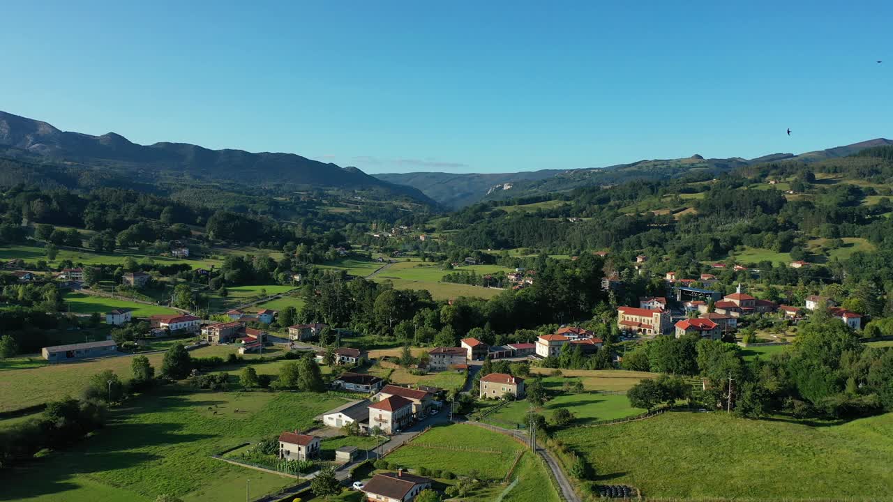vuelo de descenso con un dron en una zona rural con casas rústicas repartidas entre prados cultivados, áreas de ganado y bosques de robles con montañas en el fondo en un pueblo cantabra-basco, españa