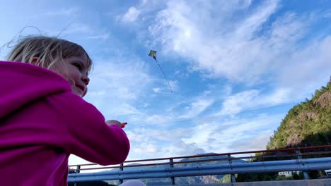 cute girl in pink playing with her kite in the wind - handheld low angle closeup of  happy girl with kite flying against bright blue sky in background