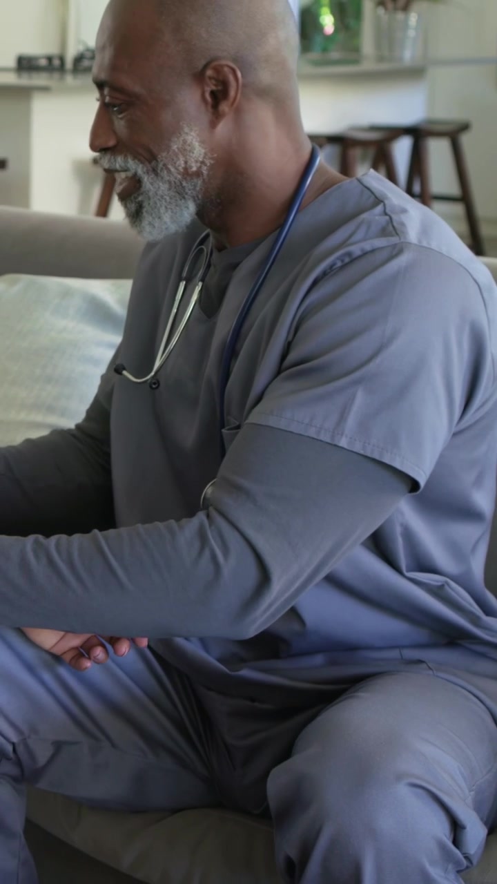 Vertical video: Inserting stethoscope senior doctor in gray scrubs at home, preparing BP cuff