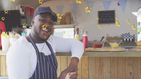 Animation-of-gold-stars-over-happy-african-american-male-food-vendor-leaning-on-counter