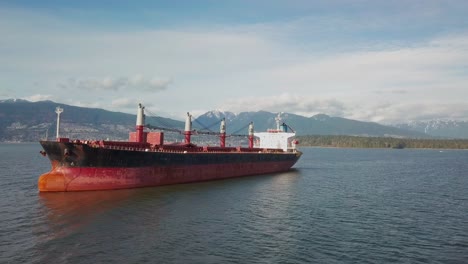 aerial shot approaching a bulk carrier ship anchored in burrard inlet near vancouver, bc, canada