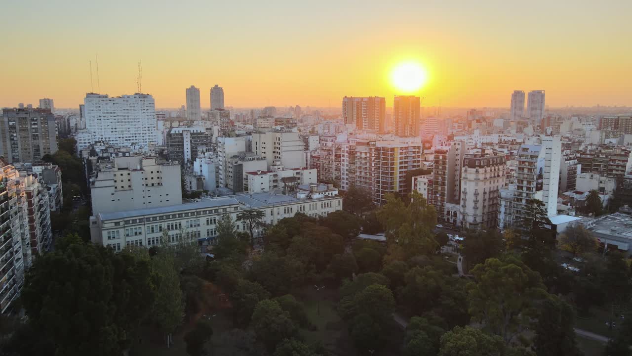 City skyline of Buenos Aires at golden hour with Parque Rivadavia tree canopy in the foreground and the sun setting in the distance. Argentina