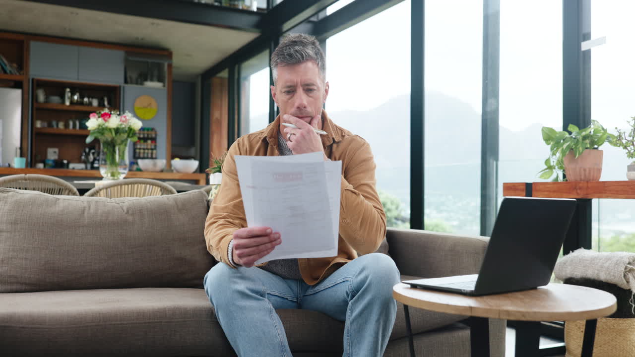 Mand sidder på sofaen og gennemgår finansielle dokumenter derhjemme