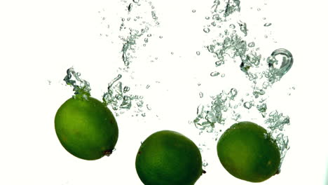 Limes-plunging-into-water-on-white-background