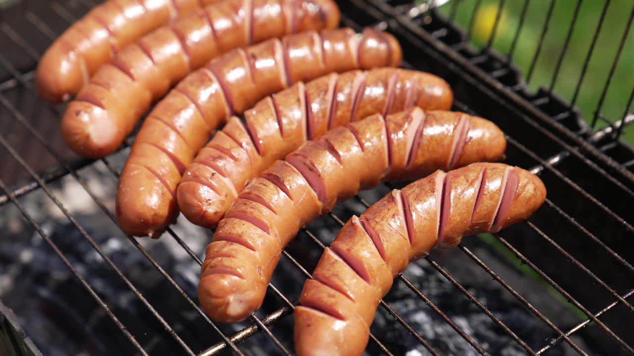 Sausages on a barbeque grill. Juicy sausages cooking over hot charcoal in smoke. Delicious food on a grill grate. Hand of chef turning sausages during cooking.