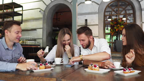 Two-girls-sitting-in-a-cafe-looking-at-the-phone-and-discuss-what-they-saw.-A-guy-comes-up-and-shows-a-funny-picture-on-his-teelphone