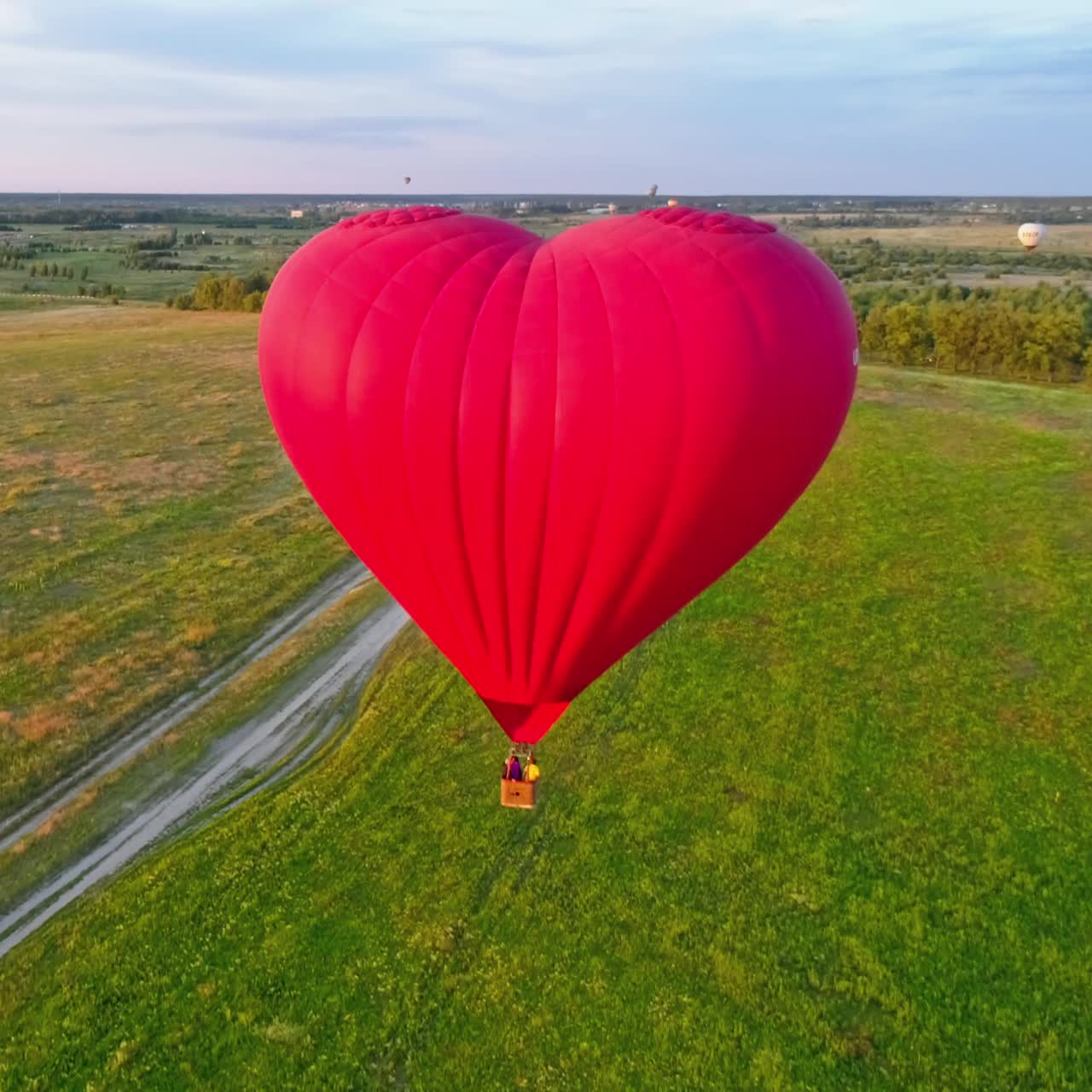 Hot air balloon flying over field. Romantic red aerostat in the heart shape moving slowly in the air. Fantastic view on the airship in summer.