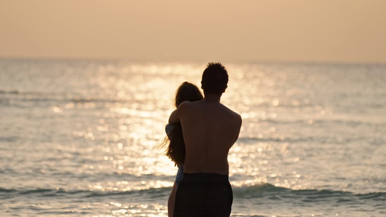 A loving pair stands barefoot on the soft white sands of Dhigurah as the sun sinks toward the horizon.