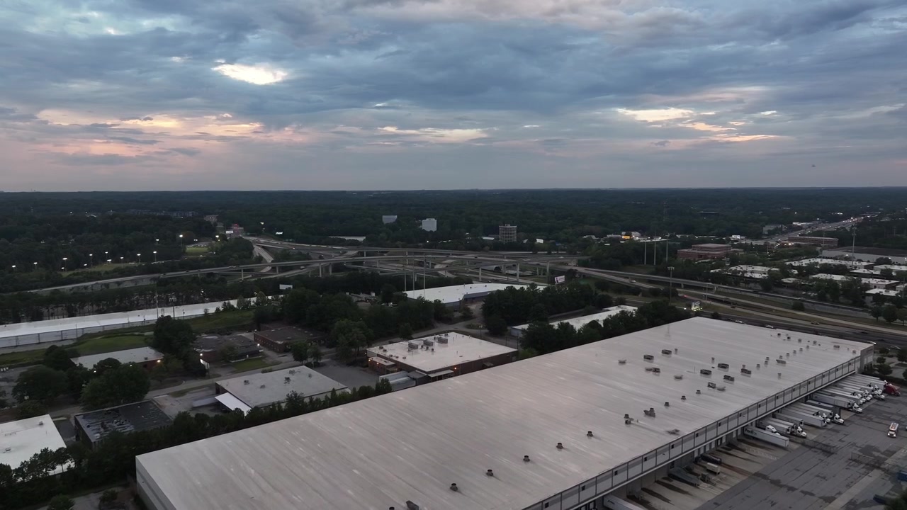 Magazzini industriali vicino a autostrada, superstrada, tangenziale, con il corridoio dello svincolo "Spaghetti Junction" sullo sfondo, vista panoramica con drone.