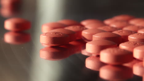 tiny pink pharmacy prescription drug pills medicine spilled across dark mirrored surface closeup