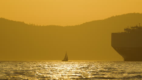 small sailboat approaching giant ocean cargo ship, golden hour glow