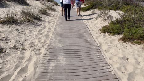 People-walking-on-wooden-path-leading-to-beach-in-Lisbon,-Portugal