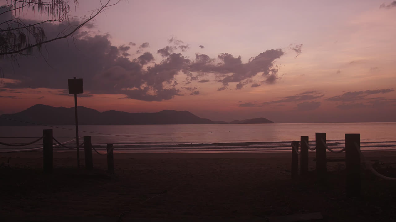 A peaceful beach sunrise looking across the rippling water with an island in the background and orange and purple sky with clouds