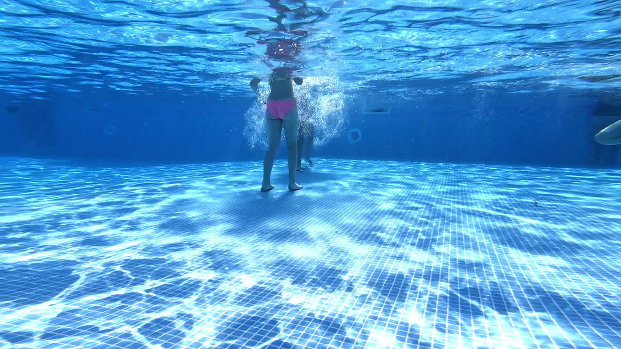 Underwater shot of girls legs playing in the pool. Children walking and waving their legs inside the swimming-pool. Clear view from underwater.