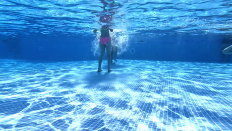 underwater shot of girls legs playing in the pool. children walking and waving their legs inside the swimming-pool. clear view from underwater.