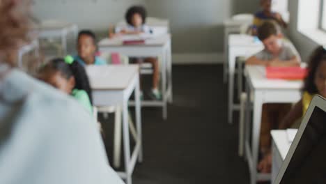 video of back view of caucasian female teacher conducting lesson in class of diverse pupils