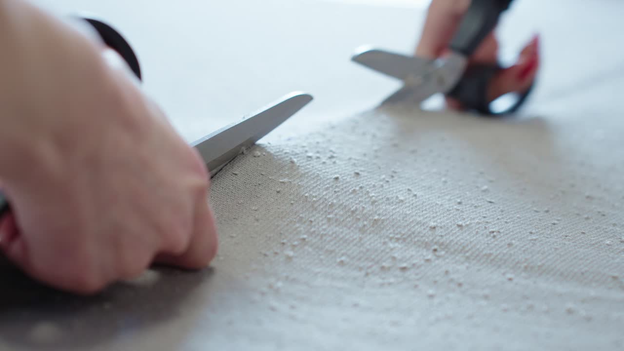 Close-up of a hand precisely cutting textured fabric with sharp scissors, capturing a moment in textile or fashion production