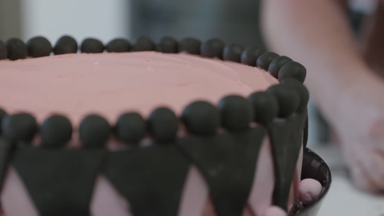 Close up, A pink and black decorated cake with a baker rolling fondant in the background