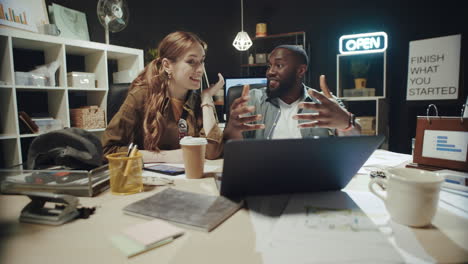 smiling african american man telling story to businesswoman near laptop indoors.