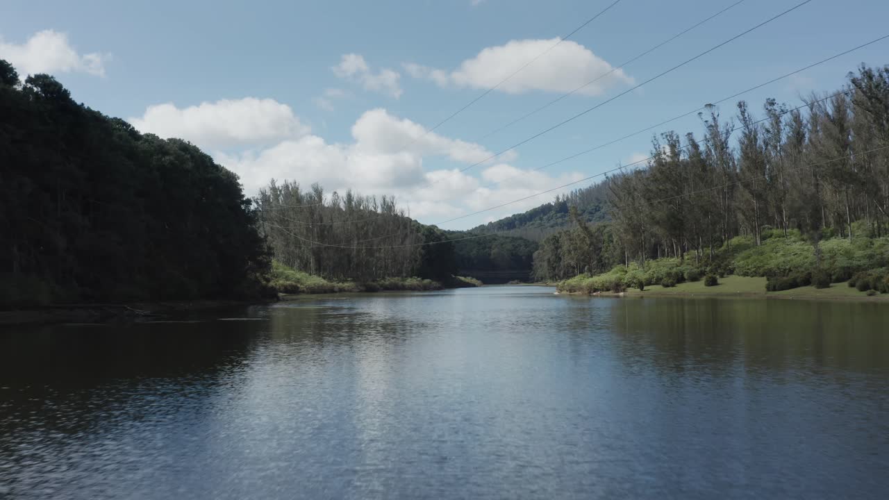 Drone pulls back over tranquil Sandynulla Lake near Sholur, Ooty, revealing forested hills and calm water surface