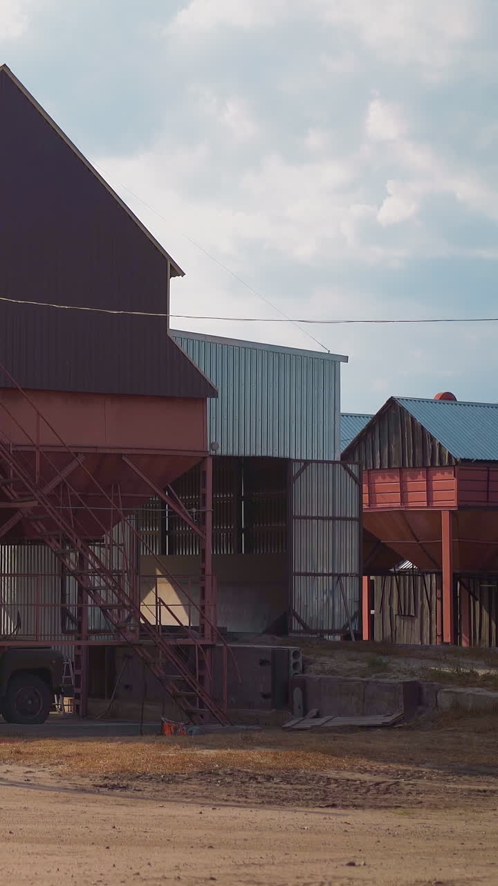 Loading grains into truck body from funnel near granary building at countryside. Wheat harvest transportation and sorting process. Agricultural industry