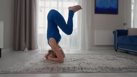 a sporty beautiful woman performs a stand on her head and hands at home. on the carpet of his own apartment. balance exercises