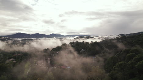 Aerial-Flight-in-sunset-through-clouds-and-mist-revealing-a-small-town-under-the-clouds-in-Valle-De-Bravo,-Mexico