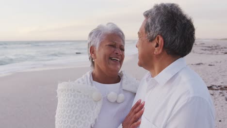 Feliz-Pareja-De-Ancianos-Hispanos-Abrazándose-Y-Riéndose-En-La-Playa-Al-Atardecer