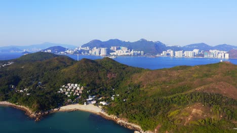 Drone-shot-traveling-upward-above-a-urbanized-tropical-island-with-some-villages-and-beach-among-the-mountains-and-forest-during-a-sunny-day