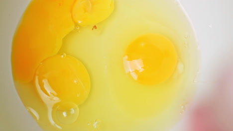 macro top shot of two raw yellow egg yolks in white dish, one egg yolk added in