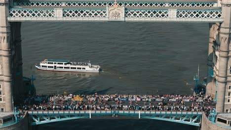 tight static shot of tower bridge with boat framed in arch and marathon runners crossing above