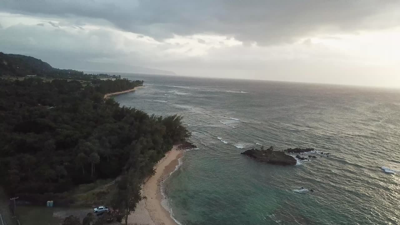 Sandy beach and waves of ocean reaching Kawela Beach in Oahu, Hawaii island. Cloudy day in summer. Aerial wide shot. Coastline and waves on tropical island