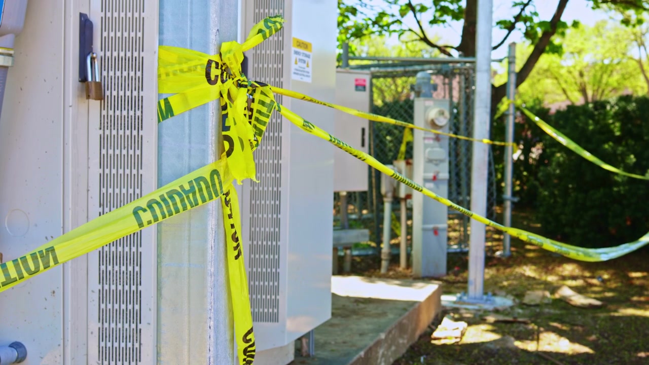 Caution tape surrounds utility equipment at a construction site in a residential area during a sunny day
