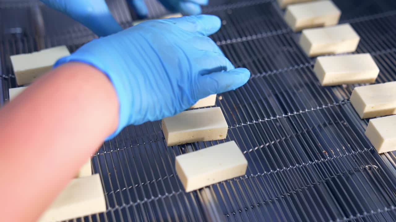 Worker's hands in blue gloves lay the sweets on the conveyor grid. Rectangular pieces of candy moving along the conveyor. Close up.