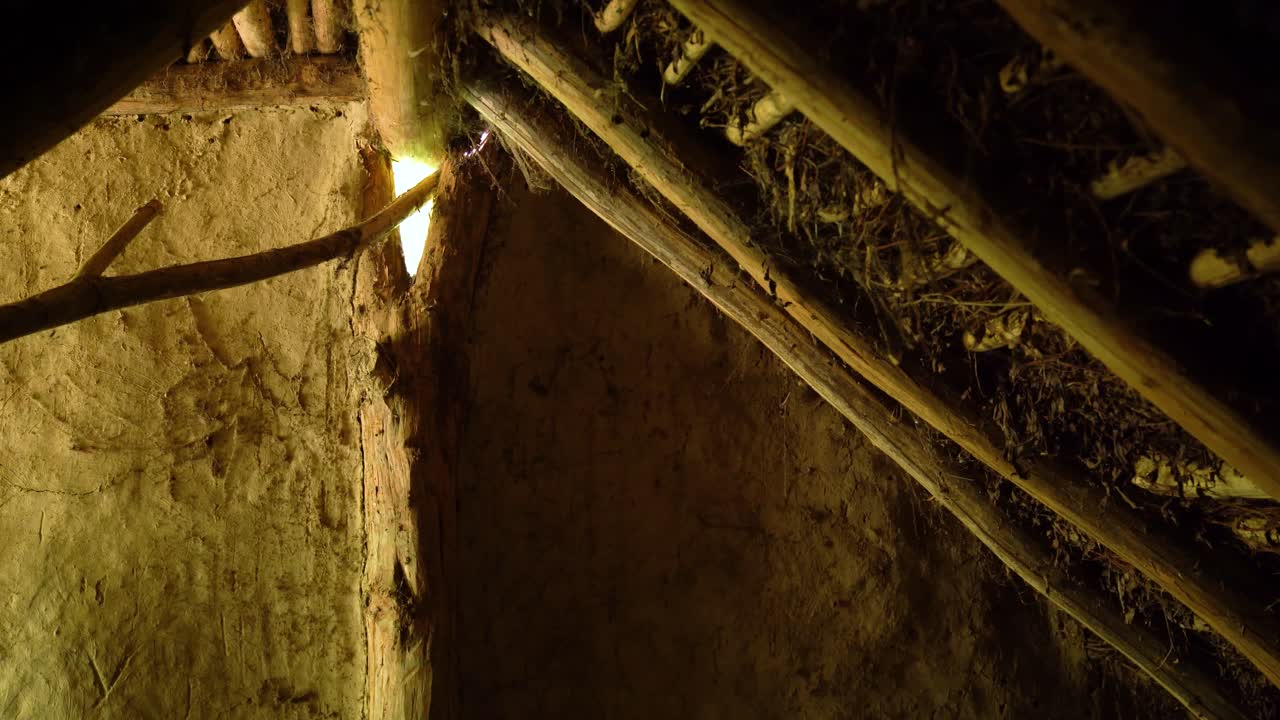 Narrow interior of an earthen house with exposed beams and patched clay walls