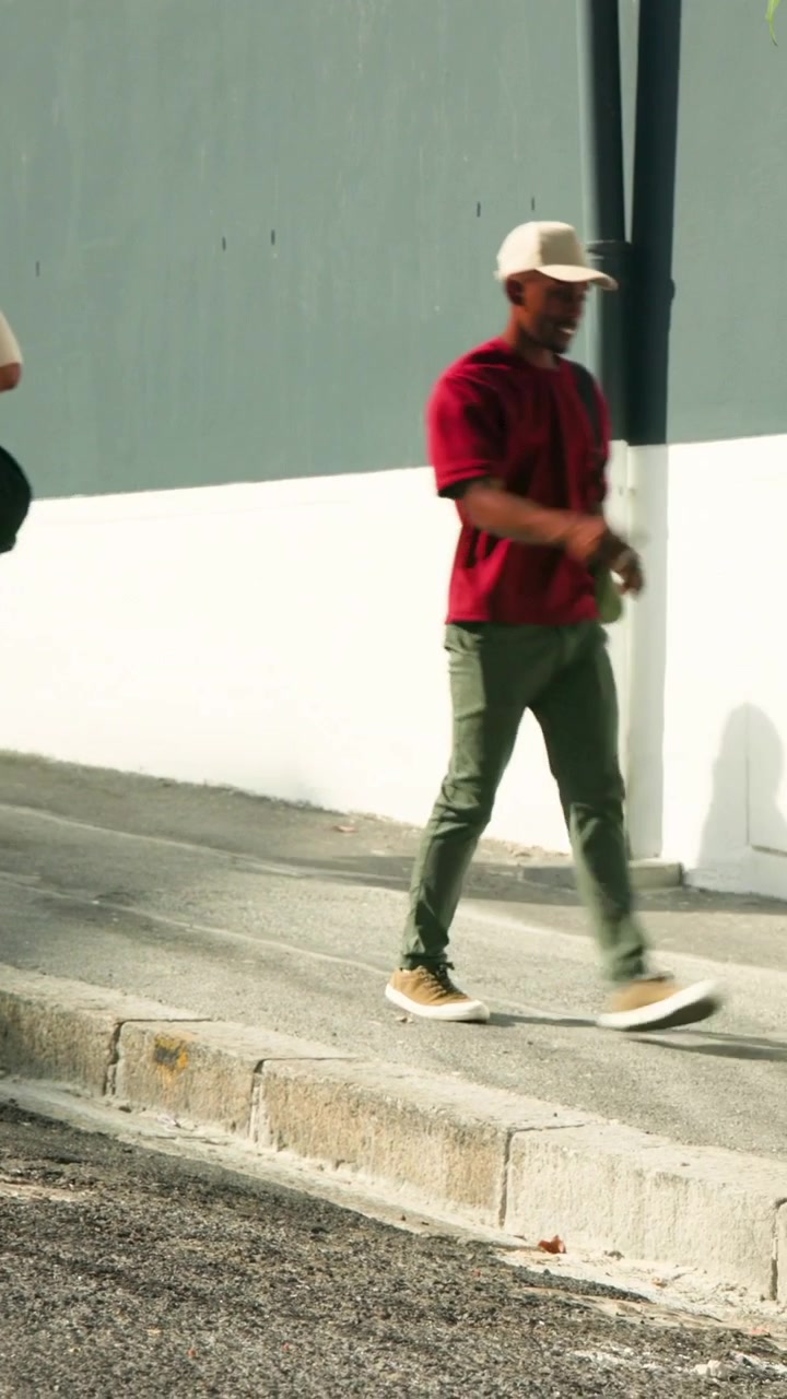 Vertical video: Starting at left edge, man in red shirt walking downhill along curb, passing duffel