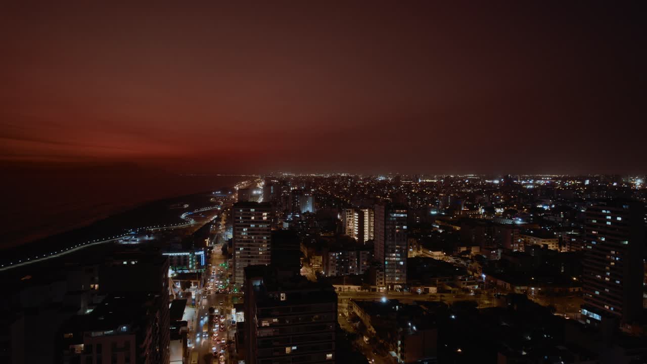 Vista aérea de una ciudad costera de noche con luces brillantes.