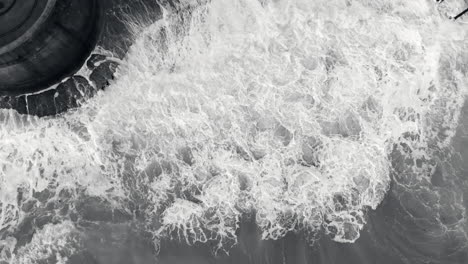 aerial footage of waves crashing against a sea wall in monochrome