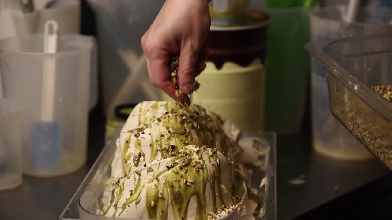 Mano che sparge pistacchi su gelato appena fatto.