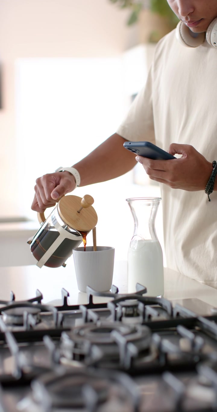Video verticale: Uomo inclina una French press, versando caffè in una tazza mentre controlla il telefono al mattino.